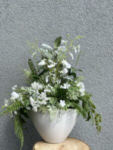 Kompozycja w białym matowym ceramicznym naczyniu z wykorzystanie białej i zielonej roślinności traw, ostów, paproci, storczyka.