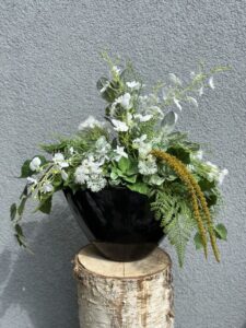 Kompozycja sztuczna wykonana z zielonych i białych roślin w czarnej ceramicznej osłonce