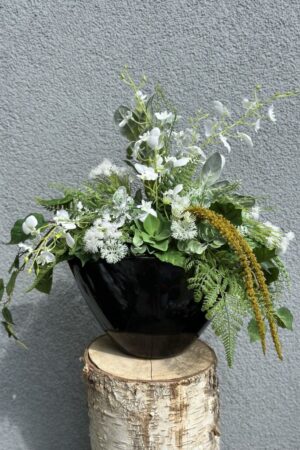 Kompozycja sztuczna wykonana z zielonych i białych roślin w czarnej ceramicznej osłonce