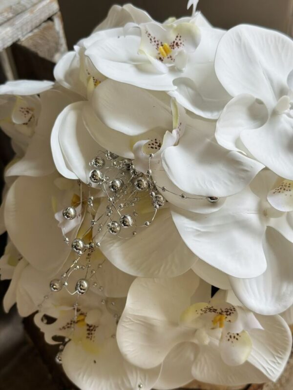 Kompozycja wykonana w ceramicznym srebrnym naczyniu z dodatkiem silikonowych kwiatów storczyka, idealna kompozycja do postawienia na stole.