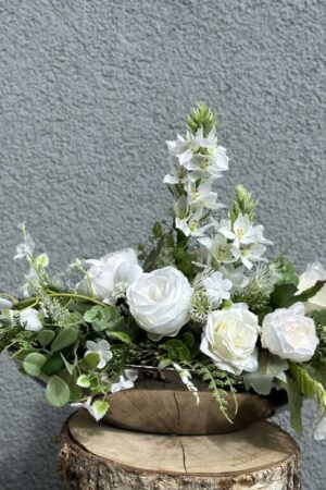 Kompozycja leżąca w srebrnym ceramicznym naczyniu z białymi kwiatami i zielonymi dodatkami.