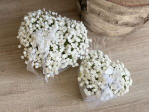 Kompozycja z sztucznych kwiatów gipsówki umieszczonych w tekturowym białym pudełku w kształcie serca.