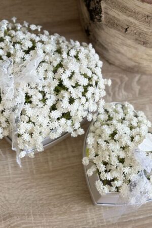 Kompozycja z sztucznych kwiatów gipsówki umieszczonych w tekturowym białym pudełku w kształcie serca.