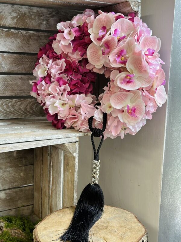 Wianek wykonany z różowych kwiatów satynowych hortensji oraz silikonowego storczyka. Dekoracja została dopełniona czarno-srebrnym chwostem.