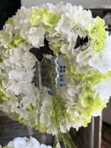 Wianek wykonany z sztucznych kwiatów biało zielonej hortensji. Dodatkiem czarne motyle oraz zielony zwis.