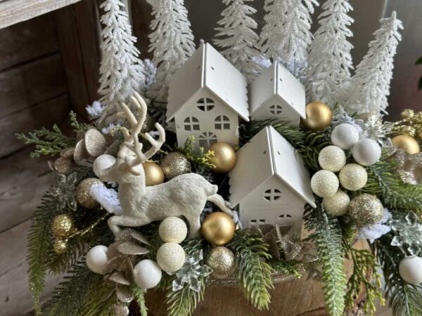 Kompozycja świąteczna wykonana na paterze ze złotą nóżką, białymi domkami, choinkami i reniferm